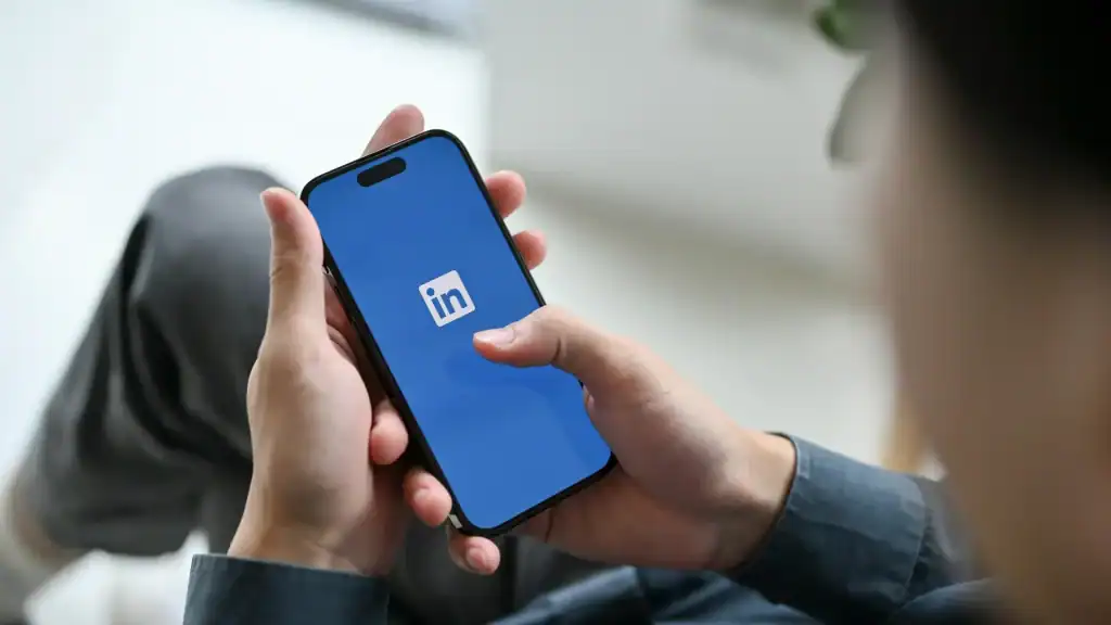 A person holding a smartphone with the LinkedIn app open on the screen, illustrating LinkedIn’s update to allow more newsworthy and discussion-based content.