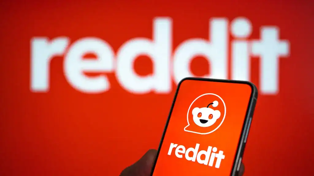 A close-up of a smartphone displaying the Reddit app with the Reddit logo in the background, representing the platform’s new automated ad targeting features.