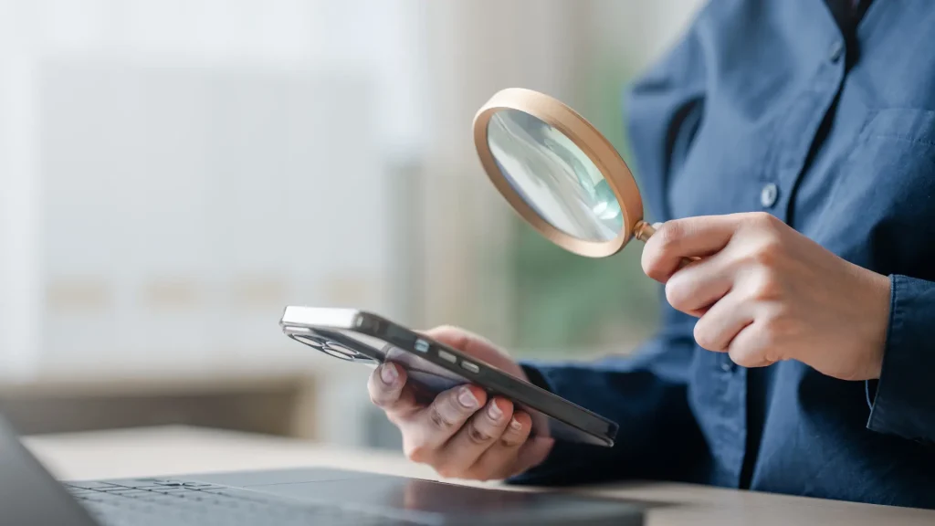 Person holding a smartphone and magnifying glass, representing keyword research focused on analysing search behaviour and user intent