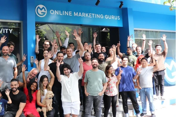 The Online Marketing Gurus Australian team gathered outside the agency's Crows Nest headquarters in Sydney, smiling and waving at the camera beneath the OMG signage.