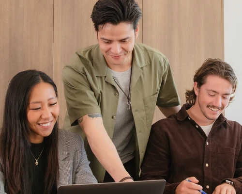 Three Online Marketing Gurus SEO migration team members collaborating around a laptop, smiling as they work through a project together.