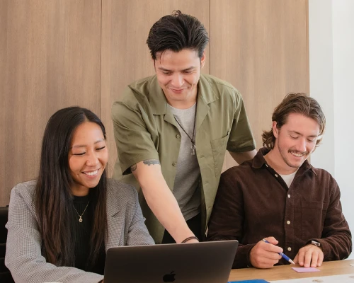 Three Online Marketing Gurus team members collaborating around a laptop, smiling as they review a WordPress and Shopify project together.