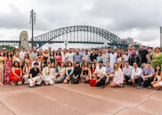 The Online Marketing Gurus Australian team posing for a large group photo at the Sydney Opera House forecourt, with the Sydney Harbour Bridge in the background.