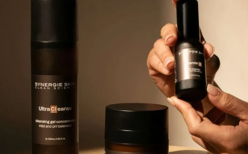 Hands holding Synergie Skin Vitamin B serum beside the UltraCleanse cleansing gel concentrate bottle.